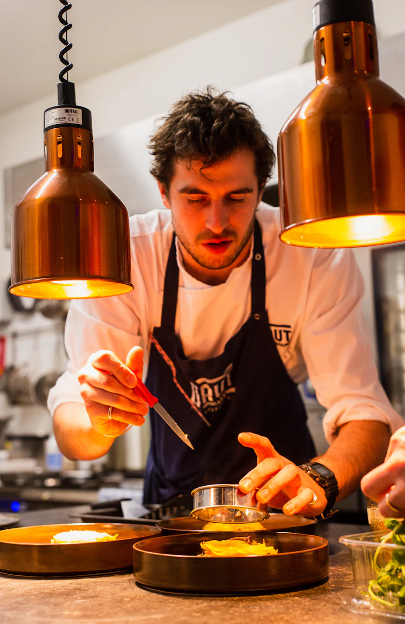 Chef plating a dish under warm copper heat lamps